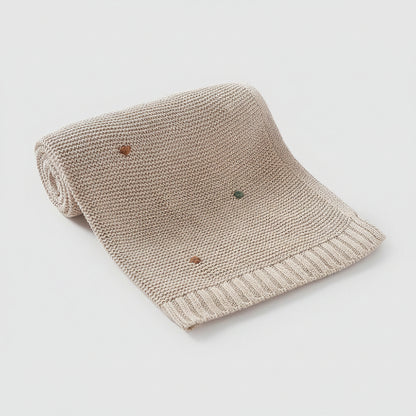 Couverture bebe tricot beige points brodés colorés enroulée fond gris clair 