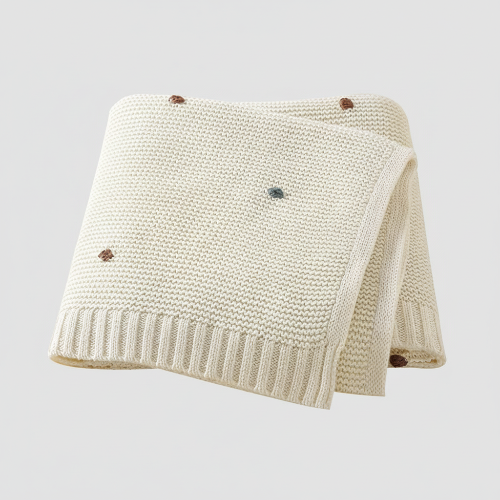 Couverture bebe tricot crème points brodés colorés pliée sur fond gris clair