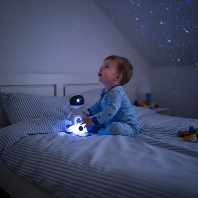 Enfant assis lit avec veilleuse projection spatiale étoiles multicolores chambre sombre
