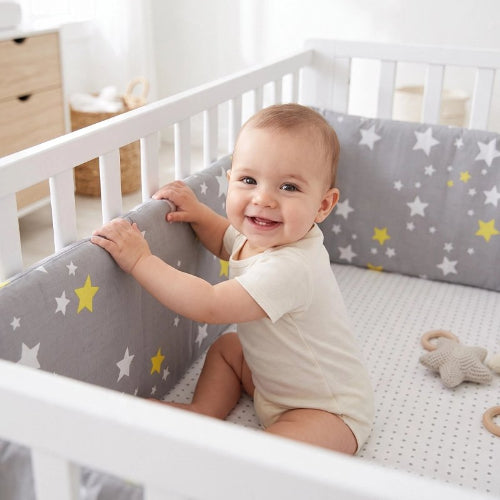 Tour de lit gris étoiles bébé souriant dans lit blanc